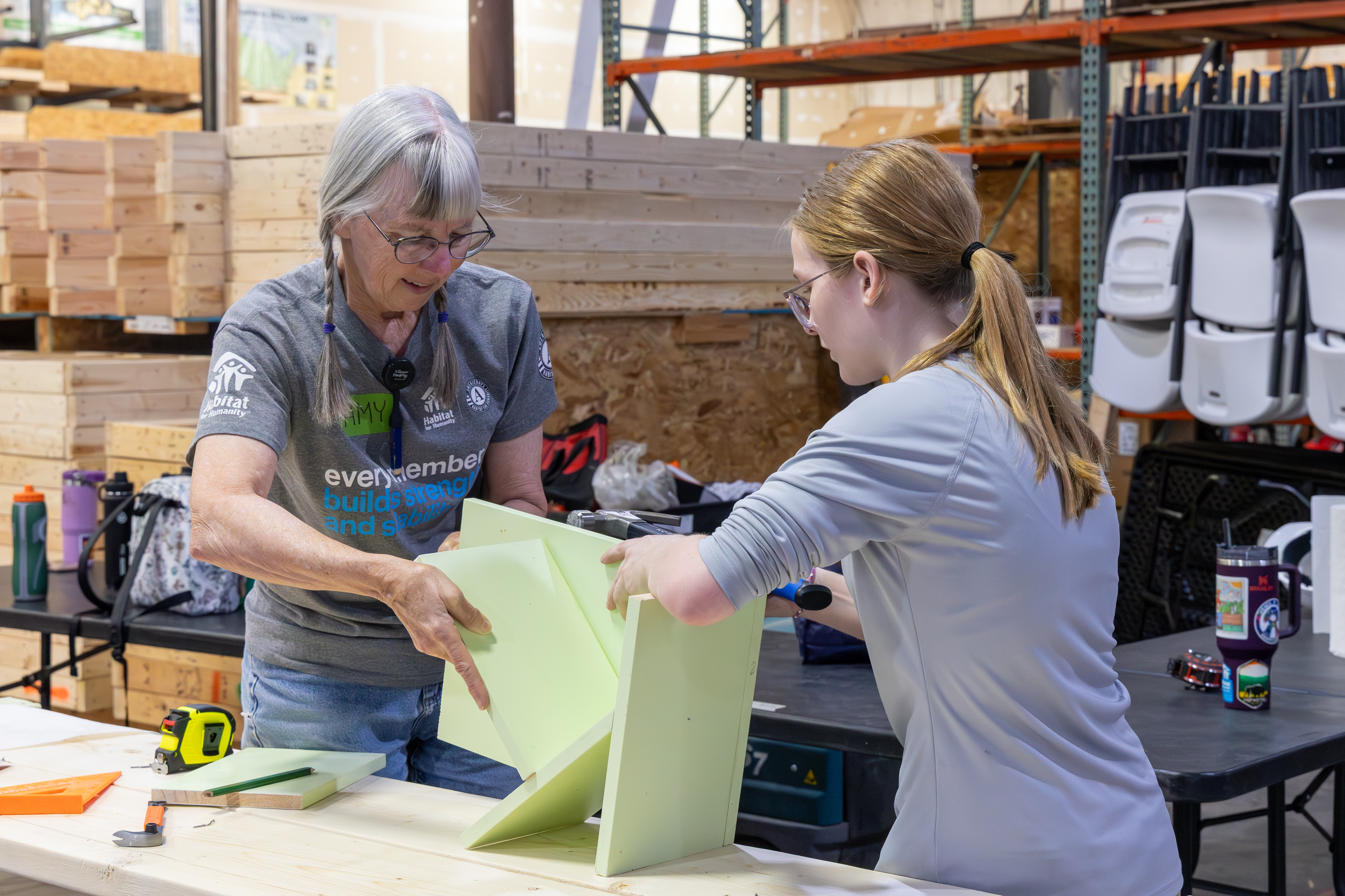 force of habitat volunteer helps summer of service intern build bookshelf