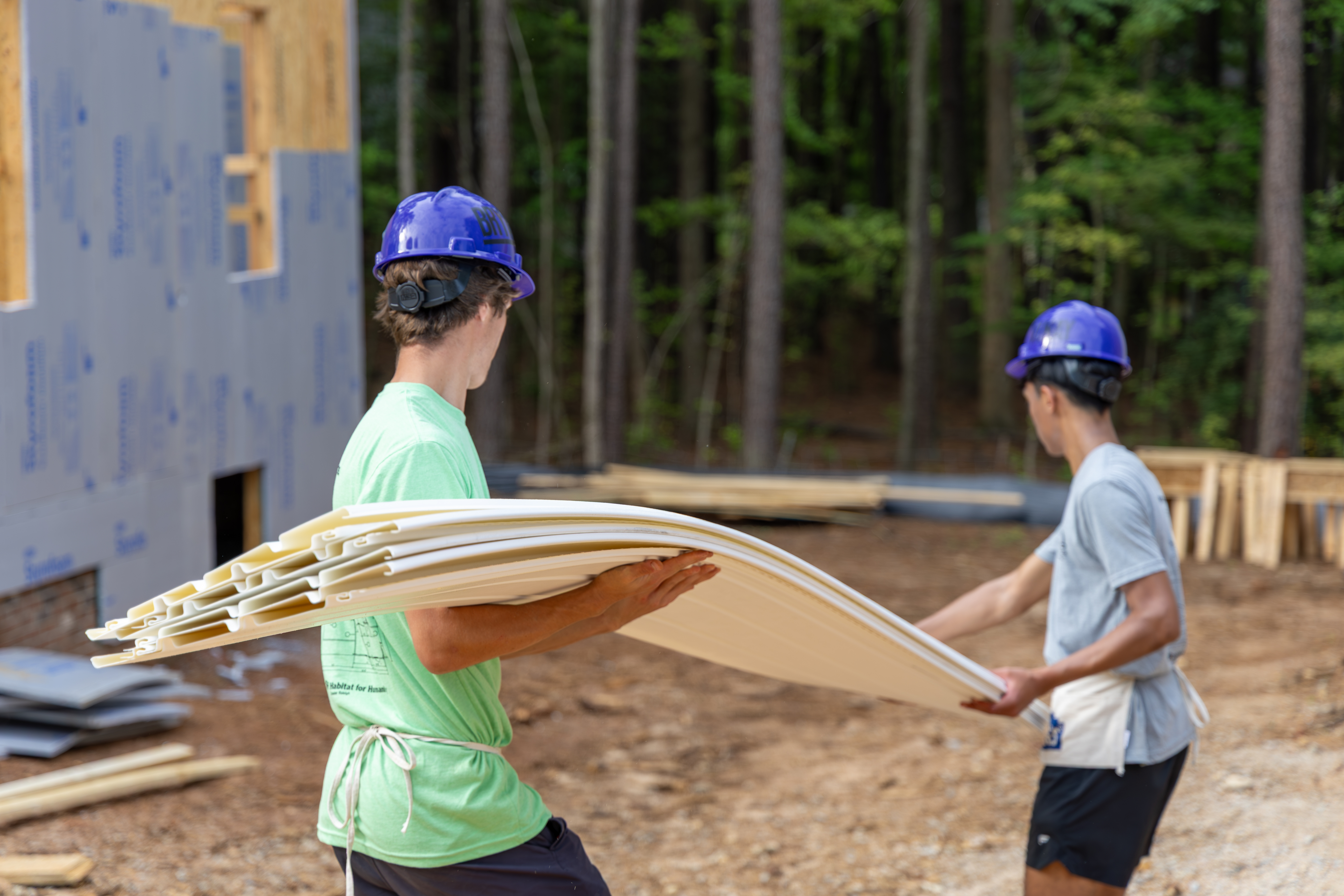 two summer of service interns carry siding on a habitat build site in wendell