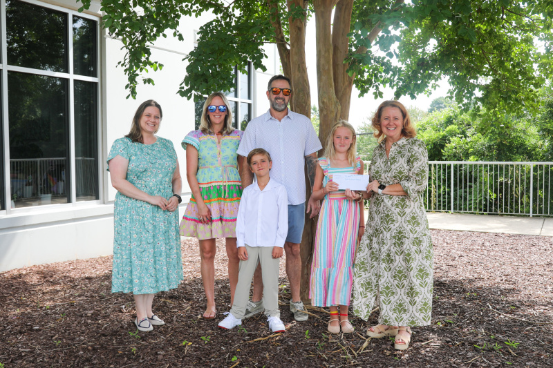Cora June and family stand outside Habitat Greater Rlaeigh office with CEO and VP of Development with check